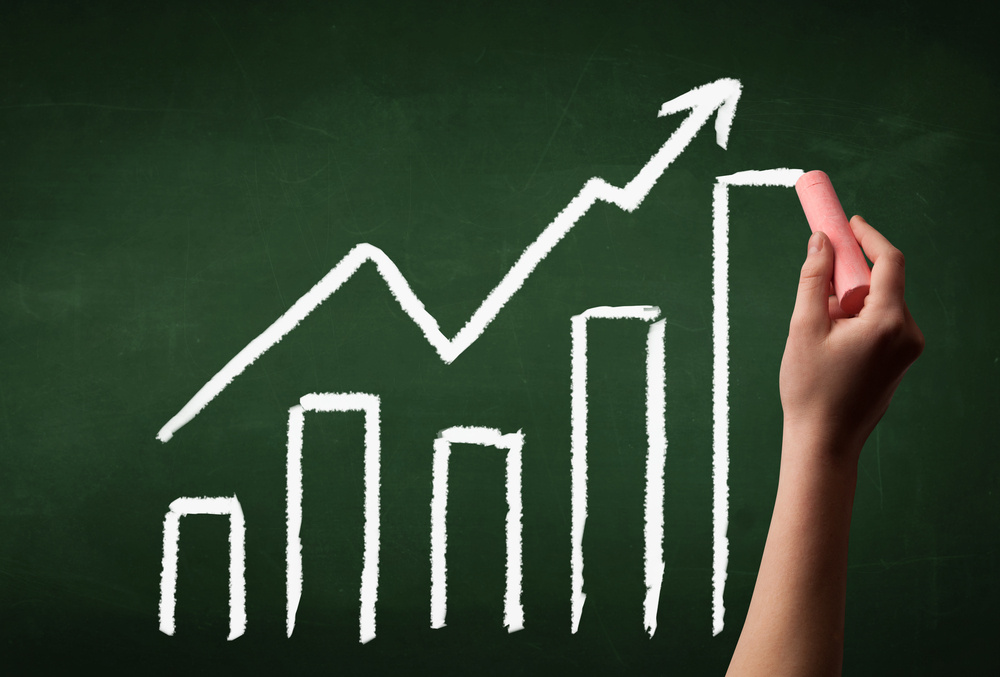A grown ups hand drawing chart with exponentially growing arrow on green chalkboard